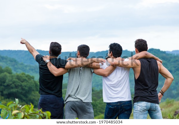 Group of male hiking and camping.\
Back view of group of young tourists man camping standing hugging\
on shoulder together and raising up his hands on mountain\

