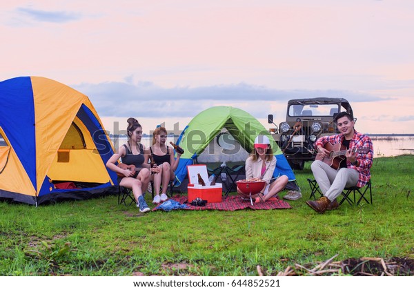 group of man and\
woman enjoy camping picnic and barbecue at lake with convertible\
off road car in\
background