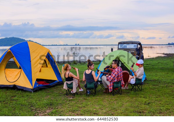 group of man and\
woman enjoy camping picnic and barbecue at lake with convertible\
off road car in\
background