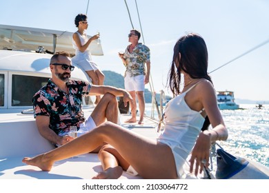 Group of man and woman friend enjoy party drinking champagne with talking together while catamaran boat sailing in summer sunny day. Male and female relax outdoor lifestyle on tropical travel vacation