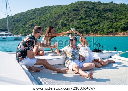 Group of man and woman friend enjoy party drinking champagne with talking together while catamaran boat sailing in summer sunny day. Male and female relax outdoor lifestyle on tropical travel vacation
