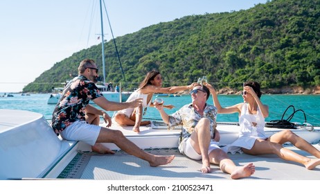 Group of man and woman friends enjoy party drinking champagne together while catamaran boat sailing in summer sunny day. Male and female relax outdoor lifestyle on sail yacht tropical travel vacation