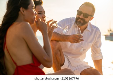 Group Of Man And Woman Friends Enjoy Party Drinking Champagne With Talking Together While Catamaran Boat Sailing At Summer Sunset. Male And Female Relax Outdoor Lifestyle On Tropical Travel Vacation