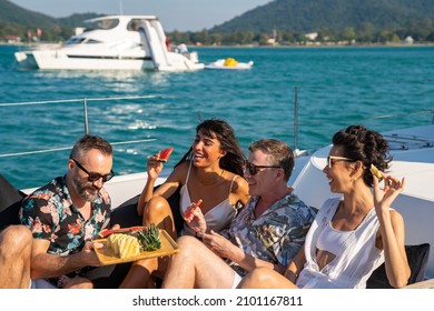 Group of man and woman friends enjoy outdoor party eating fresh fruit together while catamaran boat sailing. Male and female relax outdoor lifestyle sailing on luxury yacht on summer travel vacation