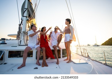 Group Of Man And Woman Friends Enjoy Party Drinking Champagne With Talking Together While Catamaran Boat Sailing At Summer Sunset. Male And Female Relax Outdoor Lifestyle On Tropical Travel Vacation