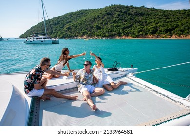 Group Of Man And Woman Friends Enjoy Party Drinking Champagne With Talking Together While Catamaran Boat Sailing At Summer Sunset. Male And Female Relax Outdoor Lifestyle On Tropical Travel Vacation