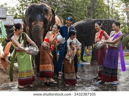 Group of man, women and children in traditional Thai costumes having fun splashing water to each other on Song kran festival in elephant camp, Chiangmai Thailand