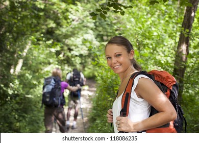 Group Of Man And Women During Hiking Excursion In Woods, With Woman Looking At Camera And Smiling. Waist Up