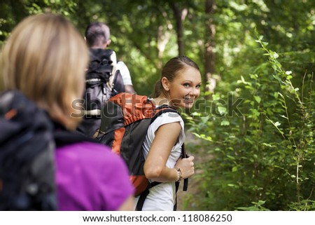 group of man and women during hiking excursion in woods, with woman looking at camera over shoulders and smiling. Waist up