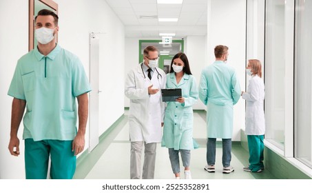 Group of masked healthcare professionals, including doctors and nurses, walk through a hospital hallway while discussing medical information and reviewing a tablet. Healthcare and teamwork concepts - Powered by Shutterstock