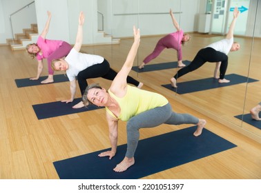 Group Of Mature Active Women Practicing Yoga, Making Together Twisting Asanas