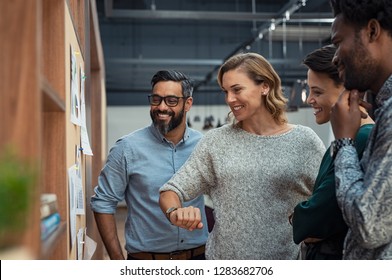 Group Of Mature Businesspeople Planning Business Strategy While Looking At Infographic On Wall. Business Men And Casual Women Looking At Pie Charts. Successful Startup Partners Feeling Happy.