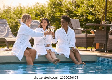 Group Of Mature Female Friends Wearing Robes Sitting With Feet In Pool Drinking Champagne On Spa Day - Powered by Shutterstock