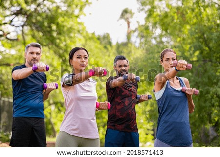 Group of mature friends exercise using dumbbells at park. Team of four middle aged people lifting weights outdoor. Determined men and fit women using dumbbell for workout in park together.