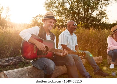 Group Of Mature Friends Sitting Around Fire And Singing Songs At Outdoor Campsite - Powered by Shutterstock