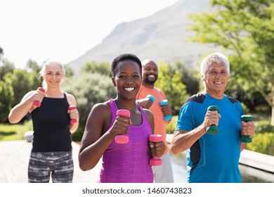 Group of mature happy people using dumbbells for workout session. Multiethnic group of smiling women and senior men exercising with dumbbells outdoor. Seniors doing workout and looking at camera. - Shutterstock ID 1460743823