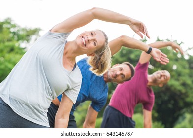 Group Of Mature Healthy People Doing Stretching At Park. Fitness Middle Aged Group Exercising Outdoor. Three Happy People In A Row Doing Stretching Arm And Smiling.
