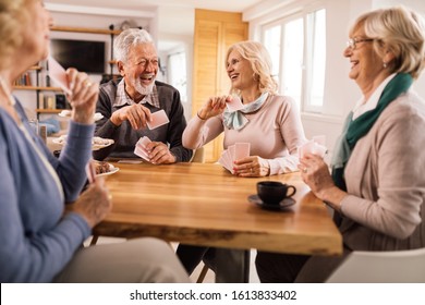 Group of mature people laughing while relaxing at home and playing cards. 