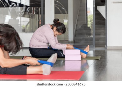 A group of mature women perform flexibility exercises, sitting on yoga mats with training bands during a pilates class. - Powered by Shutterstock