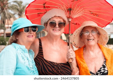 Group mature women wearing beach hats and smiling while standing on a tropical beach. Older ladies have fun in outdoor leisure activity in holiday vacation summer lifestyle. Elderly friends lifestyle - Powered by Shutterstock