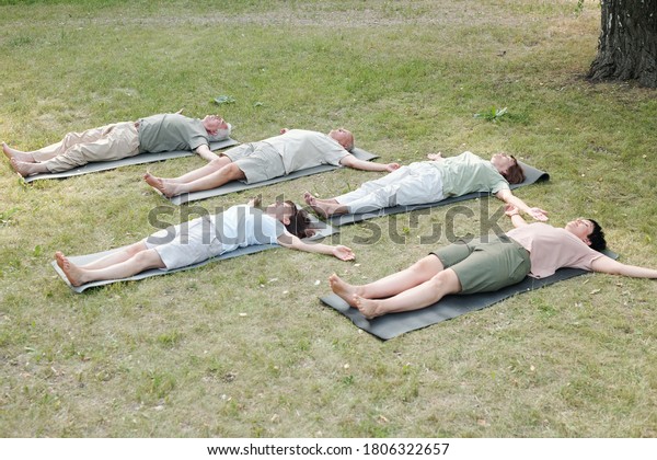 Group of mature yoga students\
lying in corpse pose on mats while resting after training in\
park