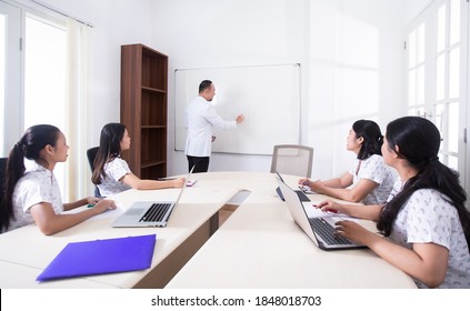 Group of medical people or nurses having business meeting, conference, seminar in office. Team members listening attentively to a cheerful doctor speaker holding a presentation standing by whiteboard - Shutterstock ID 1848018703