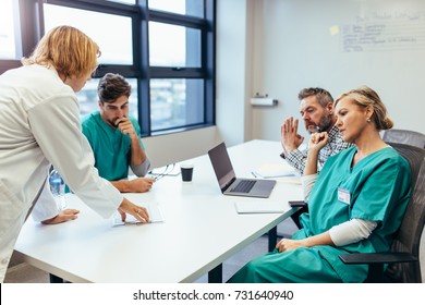 Group Of Medical Professionals Brainstorming In A Meeting. Team Of Healthcare Workers Discussing In Boardroom, With Female Doctor Presenting Her Plan.