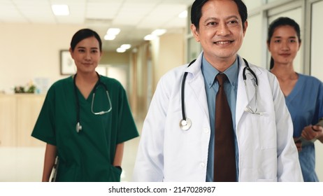 Group Of Medics Busy With Clipboard Discussing Along Hospital Corridor, Doctor And Nurse Team With Medical Report Walking Down Hallway At The Hospital