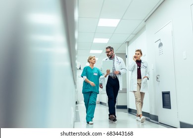 Group of medics with clipboard discussing along hospital corridor. Doctor and nurse briefing medical report with female colleague talking on mobile phone. - Powered by Shutterstock