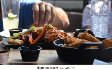 A Group Of Men Enjoy Buffalo Wings And Mozzarella Sticks At A Sports Bar.