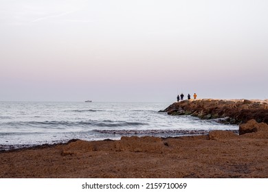 Group Of Men Fishing On The Dock At Sunset.