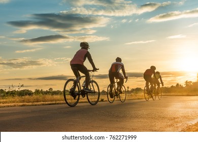 Group of  men ride  bicycles at sunset with sunbeam over silhouette trees background.