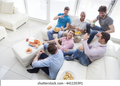 Group Of Men Sat At Home Enjoying Pizza And Beer.