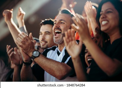Group of men and women cheering their national team. Football team supporters enjoying during watching a live match from stadium. - Shutterstock ID 1848764284