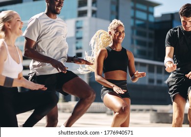 Group of men and women doing exercising together in the city. Multi-ethnic friends workout together and smiling. Running on the same place workout.