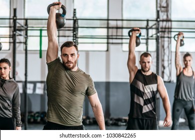 Group of men and women lifting weights at crossfit training at gym.