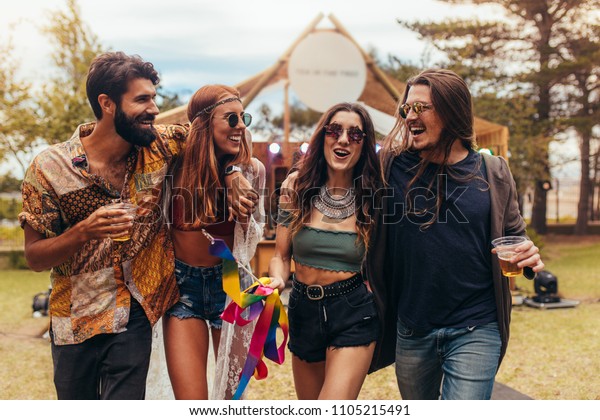 Group of men and women at music festival having\
beers and enjoying. Friends having a great time at music festival\
in a park.