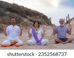 Group of men and women practicing kundalini yoga on the sand at the beach. Abhaya pose