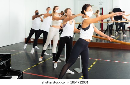 Group of men and women in protective masks practicing at the ballet barre