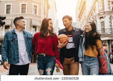 Group of men and women walking outdoors with skateboard and basketball. Two couples walking on city street. - Shutterstock ID 1335365528