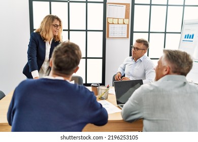 Group Of Middle Age Business Workers Listening Boss Speech During Meeting At The Office.