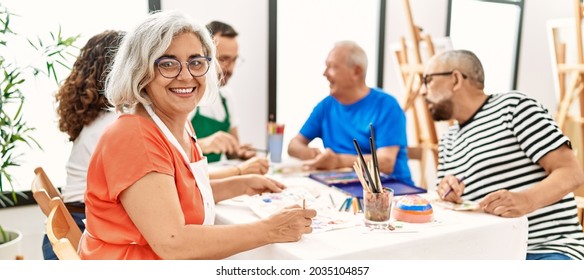 Gruppen mittleren Alters ziehen Studenten, die auf dem Tisch sitzen und im Kunststudio zeichnen. Frauen lächeln glücklich, wenn sie die Kamera sehen.