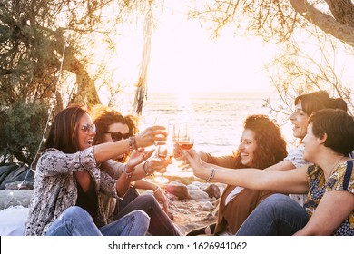 Group Of Middle Age Young Adult Women Having Fun Together Toasting And Clinking With Wine Glasses At The Beach During A Golden Sunset Enjoying Outdoor Leisure Activity Or Vacation