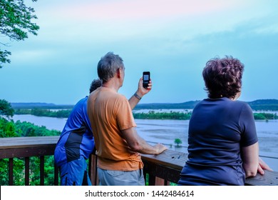 Group Of Middle Aged People Enjoying View Of Missouri River Flood Plain From Observation Deck In The Evening; One Man Taking Photos With His Smartphone; Blue Sky In Background