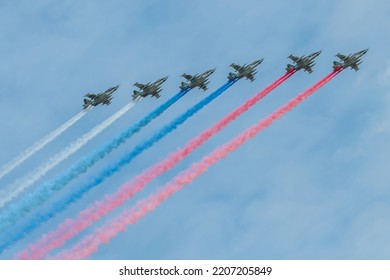 Group of military aircrafts flies in formation with three colored smoke in shape of russian flag in the sky during Victory Day parade in Russia.