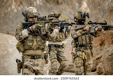 A group of military men in combat gear patrol in the middle of a desert and tropical jungle. Soldiers in full combat gear in dry weather conditions assemble and march on a mission.