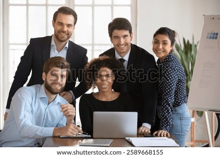 Group of millennial multinational teammates posing for camera in modern conference room. Portrait of five successful, motivated, skilled staff members working on joint online project in company office