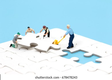 Group of miniature people assembling jigsaw puzzle, team support and help concept. Business teamwork concept.