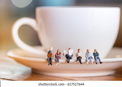 Group of miniature people figures sitting, waiting and reading newspaper and book on white plate of cup of hot coffee at coffee shop. - Powered by Shutterstock