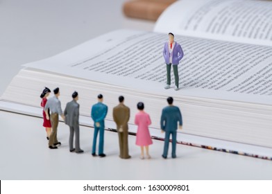 Group of miniature people holding a meeting with the leader standing on an open book and the other men and women gathered below - Shutterstock ID 1630009801